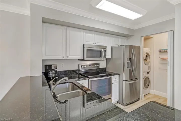 Kitchen featuring ornamental molding, stainless steel appliances, white cabinetry, light wood-type flooring, and dark stone countertops