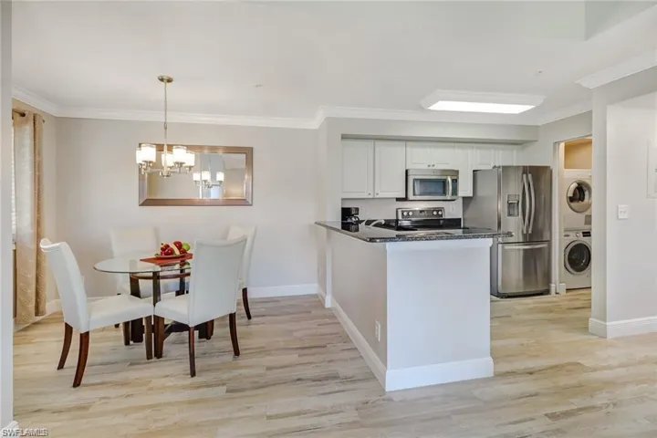 Kitchen with stainless steel appliances, ornamental molding, a peninsula, white cabinetry, and dark stone counters