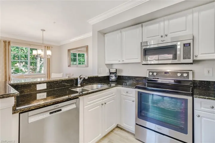 Kitchen featuring stainless steel appliances, white cabinets, dark stone countertops, ornamental molding, and a peninsula