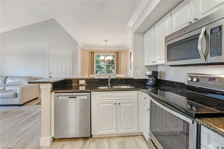 Kitchen with stainless steel appliances, white cabinets, dark stone countertops, ornamental molding, and open floor plan