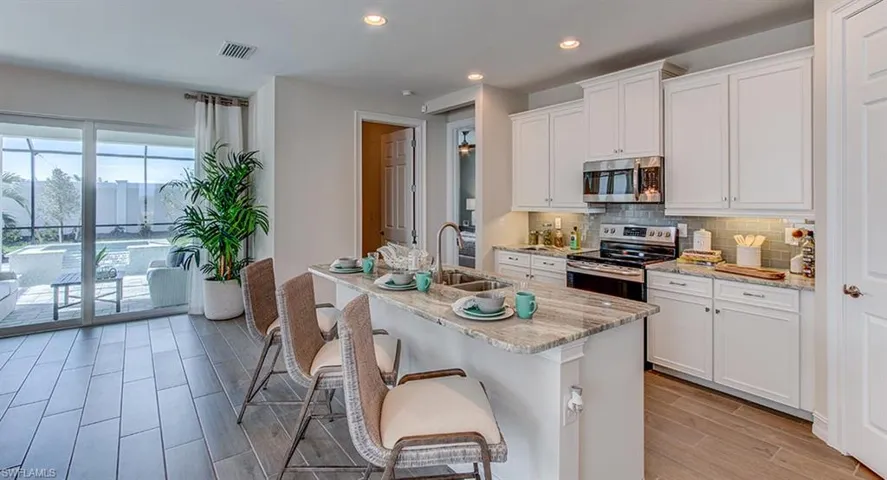 Kitchen with light stone countertops, tasteful backsplash, an island with sink, white cabinetry, and appliances with stainless steel finishes