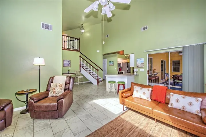 Living area with a towering ceiling, ceiling fan, stairway, and marble finish flooring