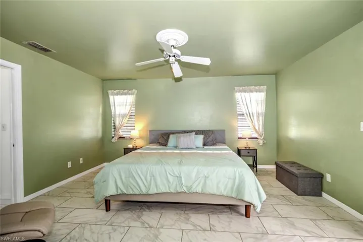 Bedroom with a ceiling fan, multiple windows, and marble look tile flooring