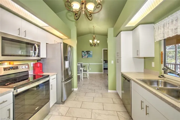 Kitchen with appliances with stainless steel finishes, white cabinets, light countertops, decorative light fixtures, and a chandelier