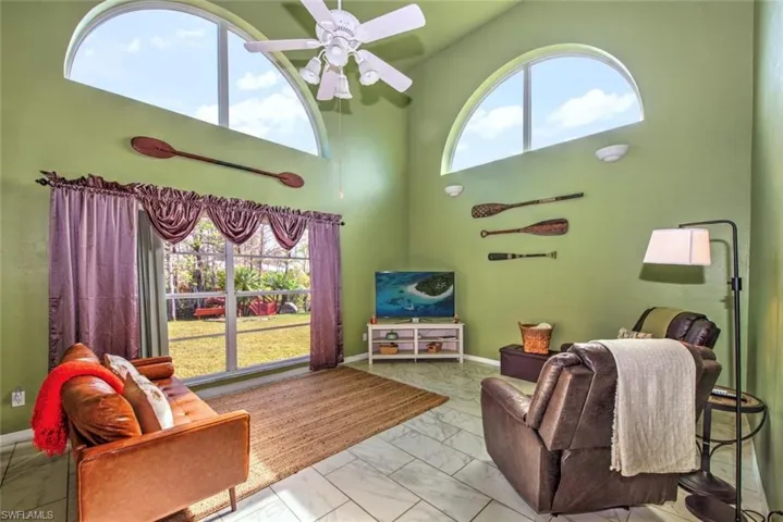 Living room with marble look tile flooring, plenty of natural light, ceiling fan, and a high ceiling