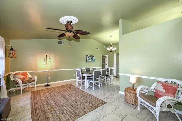 Sitting room with lofted ceiling, light marble finish floors, a ceiling fan, and a chandelier