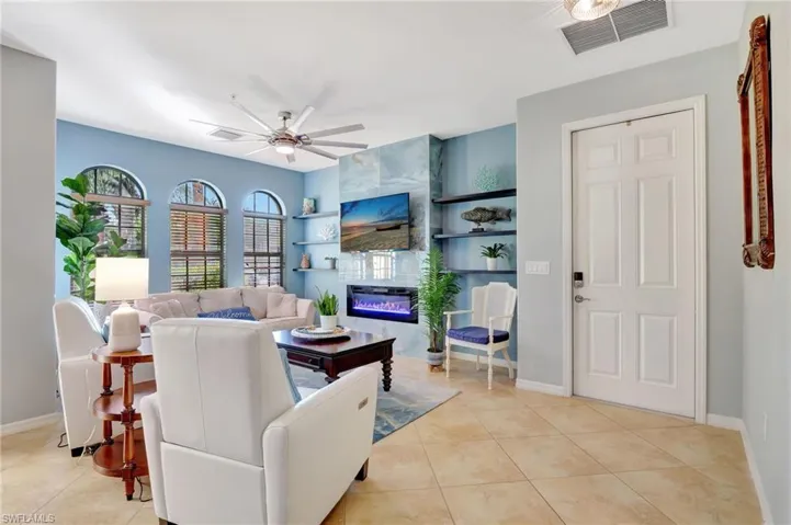 Living room with a tiled fireplace, ceiling fan, and light tile patterned floors