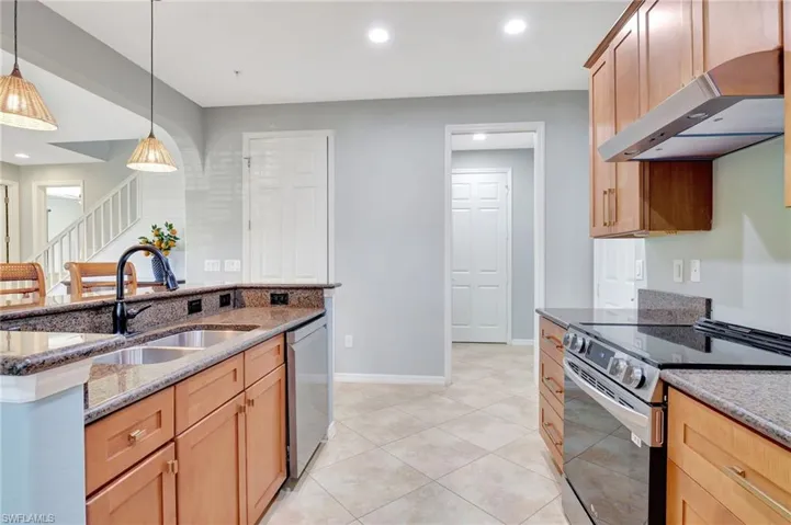 Kitchen with dark stone countertops, ventilation hood, pendant lighting, and stainless steel appliances