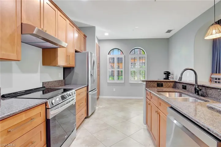 Kitchen with decorative light fixtures, stainless steel appliances and dark stone counters