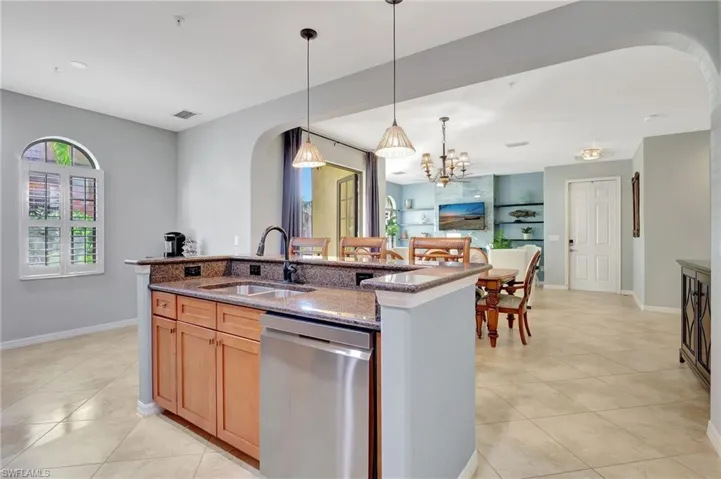 Kitchen with stainless steel dishwasher, dark stone counters, and  island with sink