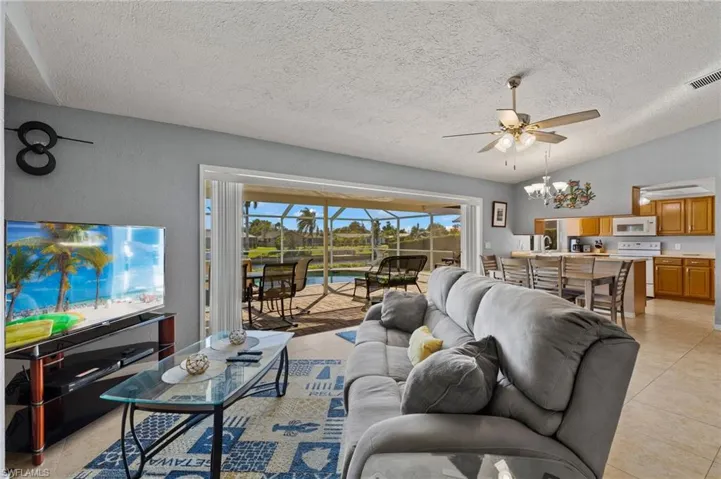 Tiled living room with ceiling fan with notable chandelier, a textured ceiling, a water view, and vaulted ceiling