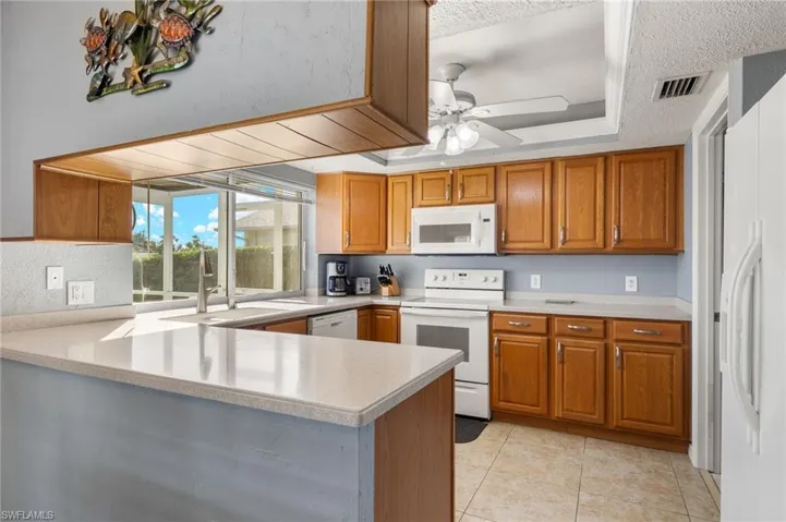 Kitchen with ceiling fan, sink, kitchen peninsula, white appliances, and light tile patterned floors