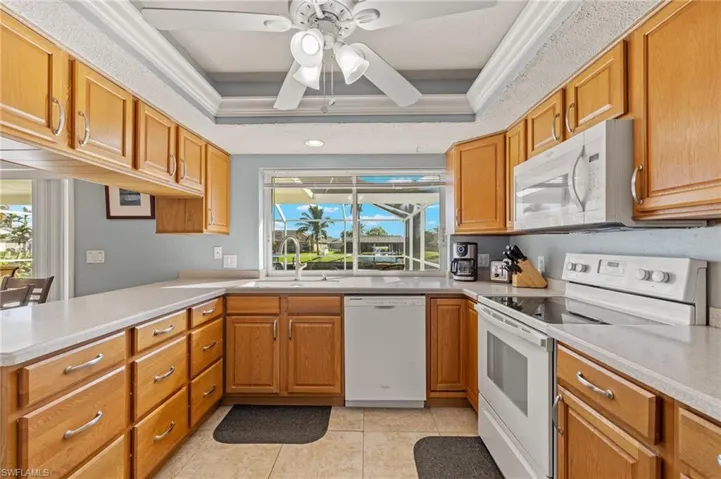 Kitchen featuring white appliances, sink, light tile patterned floors, and a tray ceiling