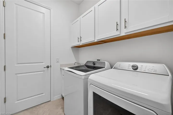 Laundry room featuring washer and dryer, cabinet space, and light tile patterned floors
