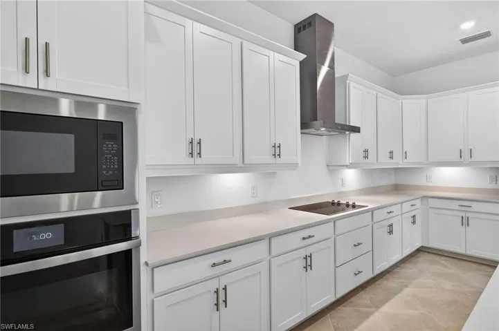 Kitchen featuring stainless steel appliances, wall chimney exhaust hood, and white cabinetry