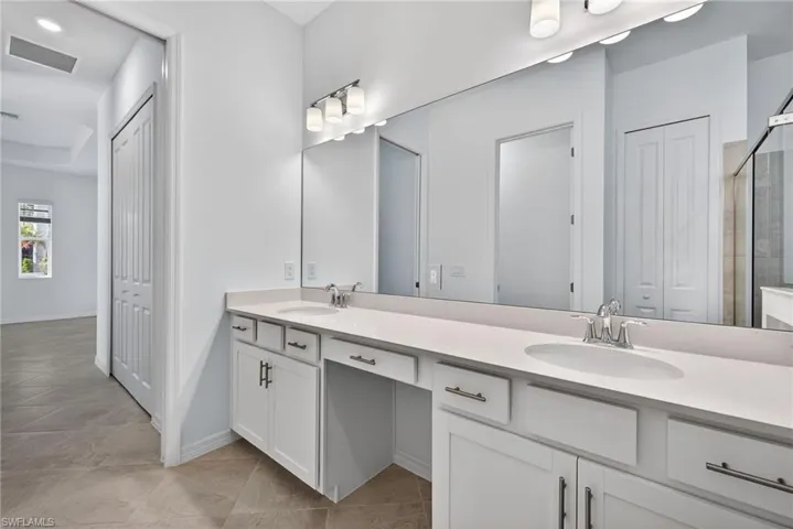 Primary Bathroom with a closet, double vanity, recessed lighting, light tile patterned floors, and a tile shower