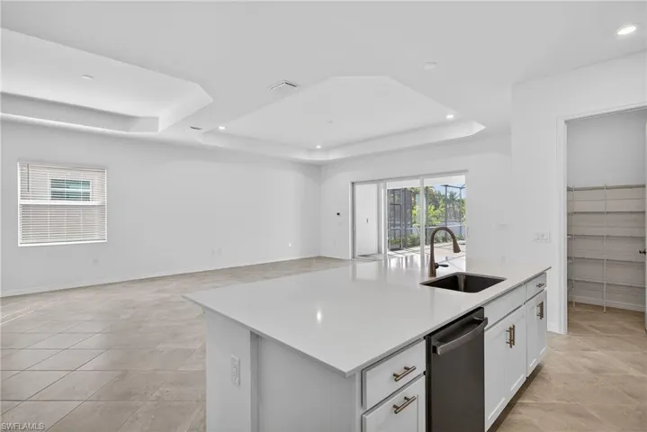 Kitchen featuring an island with sink, light stone counters, stainless steel dishwasher, open floor plan, and a tray ceiling