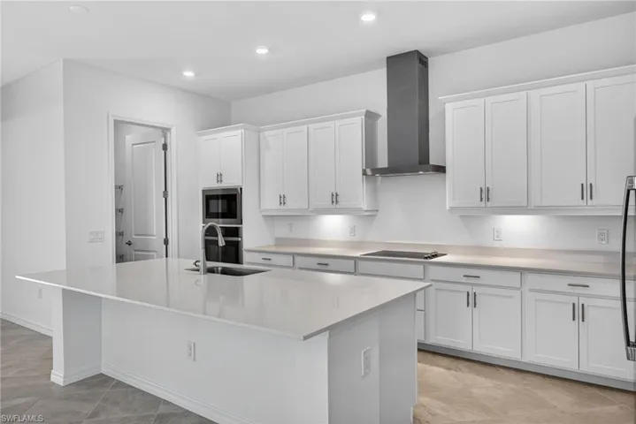 Kitchen with white cabinetry, stainless steel appliances, light stone counters, a kitchen island with sink, and recessed lighting