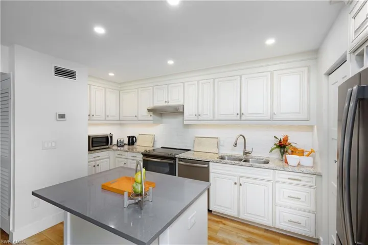 Kitchen featuring appliances with stainless steel finishes, light hardwood / wood-style flooring, sink, a kitchen island, and white cabinetry