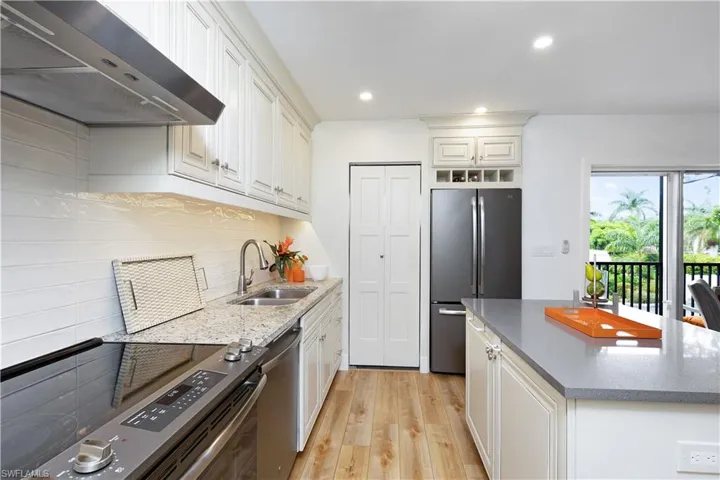 Kitchen with tasteful backsplash, light hardwood / wood-style flooring, wall chimney exhaust hood, and sink