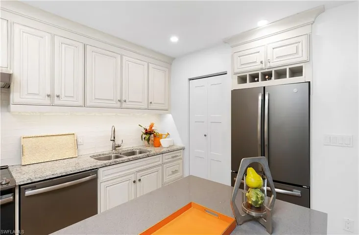 Kitchen with white cabinetry, stainless steel appliances, sink, light stone counters, and backsplash