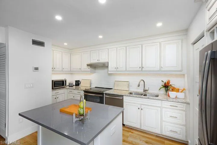 Kitchen with stainless steel appliances, white cabinets, sink, a kitchen island, and light wood-type flooring