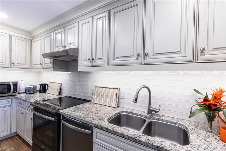 Kitchen featuring backsplash, light stone counters, stainless steel appliances, hardwood / wood-style flooring, and sink
