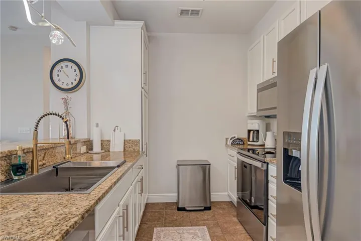 Kitchen featuring stainless steel appliances, white cabinets, light stone counters, pendant lighting, and a chandelier