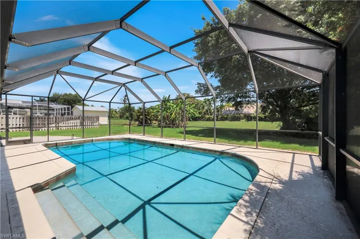 Screen-enclosed swimming pool featuring a curved design, integrated steps, and light-colored concrete decking