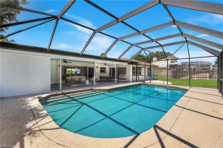 Covered dining and social area inside a screened lanai with a swimming pool and concrete pool deck.