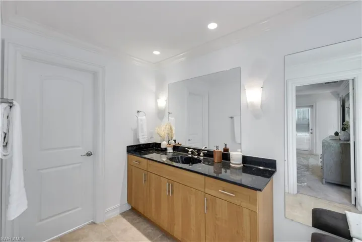 Primary bathroom with wood vanity with sinks, black stone countertop, and an wall-mounted mirrors.