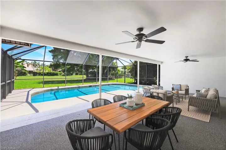 Covered dining and social area inside a screened lanai with a swimming pool, concrete pool deck, two ceiling fans.