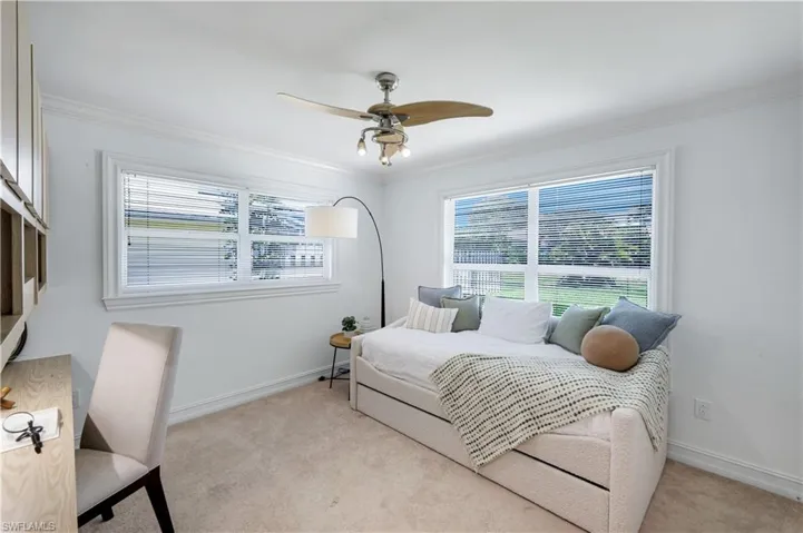 Bedroom #3 featuring a ceiling fan with integrated lighting, two large windows with blinds, built-in shelving, and neutral carpet.