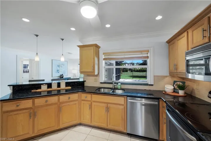 Kitchen with wood cabinetry, granite countertops, stainless steel appliances, and pass through window into the lanai area.