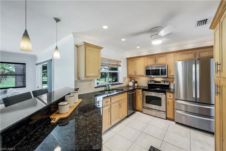 Kitchen with wood cabinetry, granite countertops, stainless steel appliances, and pass through window into the lanai area.