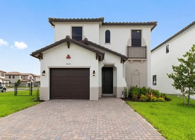 Contemporary stucco residence featuring a paver driveway, an attached garage, and a second-story balcony with iron railing