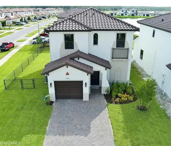 Spanish Colonial style architecture with a tile roof, an integrated one-car garage, a paver driveway, an upper-level balcony, and mature landscaping