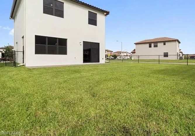 Expansive green lawn bordering a two-story stucco exterior featuring multiple windows with dark frames, a sliding glass door, and a tiled roof