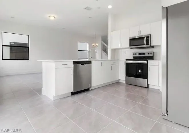 Modern kitchen featuring white cabinetry, stainless steel appliances, a center island with integrated dishwasher, and tile flooring