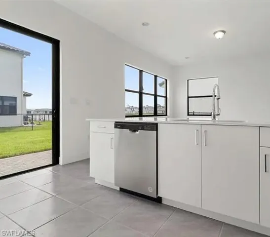 Kitchen featuring white cabinetry, light-toned countertops, a stainless steel dishwasher, and a gooseneck faucet