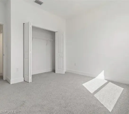 Carpeted room featuring a bifold door closet with shelving, white painted walls, and white baseboards