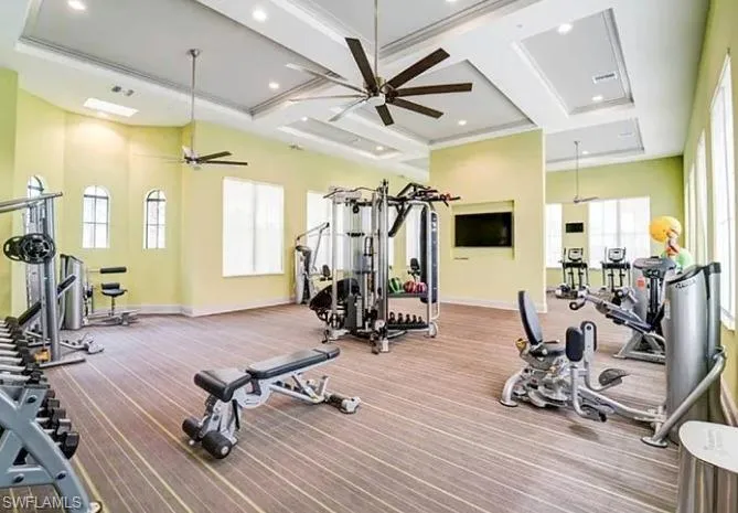 Spacious fitness room featuring a coffered ceiling, ceiling fans, recessed lighting, and multiple windows providing natural illumination
