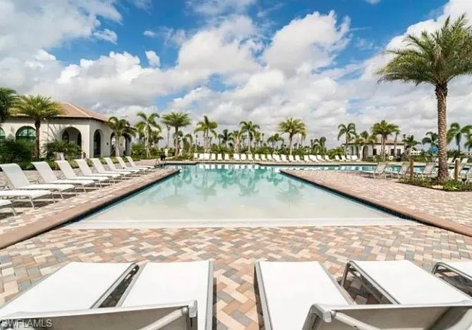 Spacious outdoor swimming pool surrounded by a paver deck, multiple lounge chairs, and mature palm trees