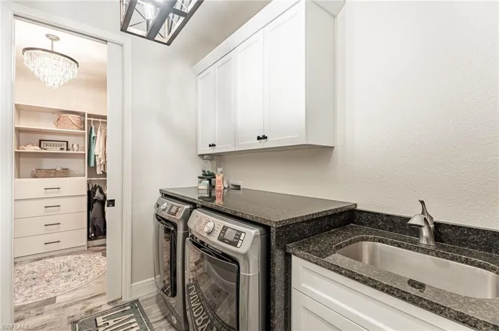 Clothes washing area with hardwood / wood-style floors, a notable chandelier, sink, separate washer and dryer, and cabinets
