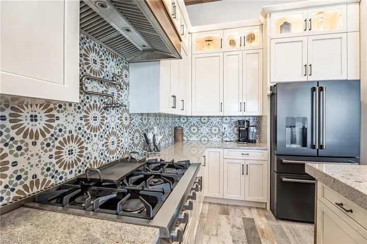 Kitchen featuring custom range hood, light hardwood / wood-style flooring, gas range, tasteful backsplash, and high quality fridge