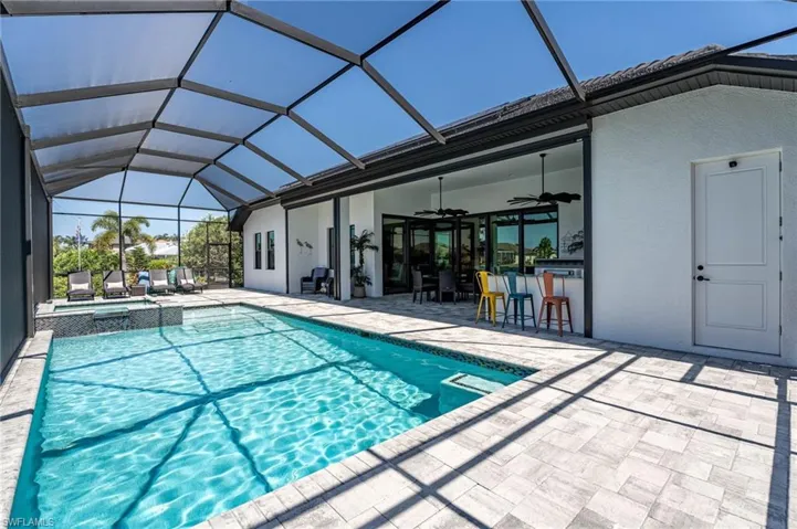 View of swimming pool and spa with pavers, an outdoor kitchen and ceiling fans.