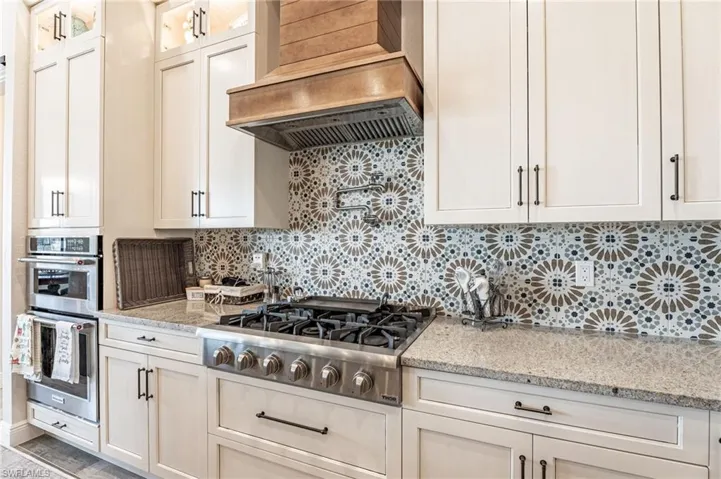 Kitchen with stainless steel appliances, light stone counters, custom range hood, and tasteful backsplash