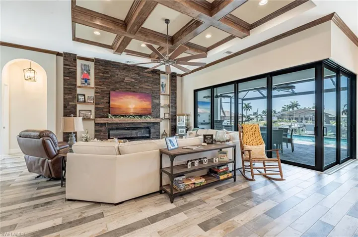 Living room with light wood-type flooring, a stone fireplace, ceiling fan, and coffered ceiling