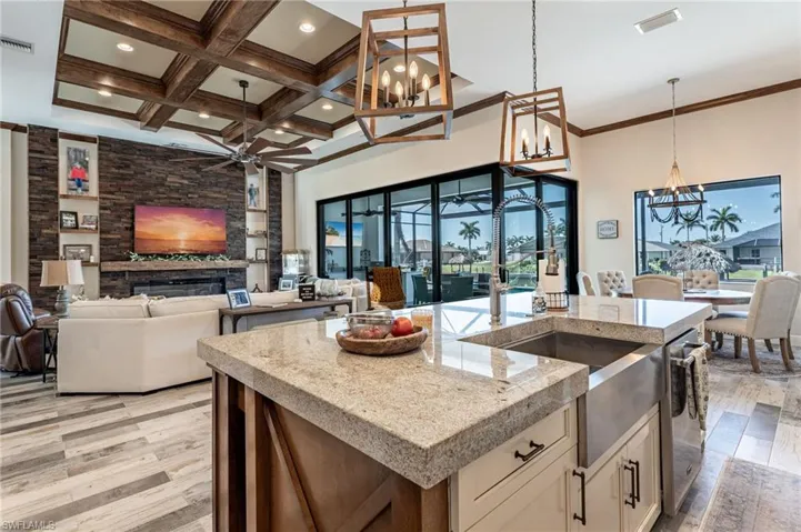 Kitchen with decorative light fixtures, a stone fireplace, an island with sink, and light wood-type flooring