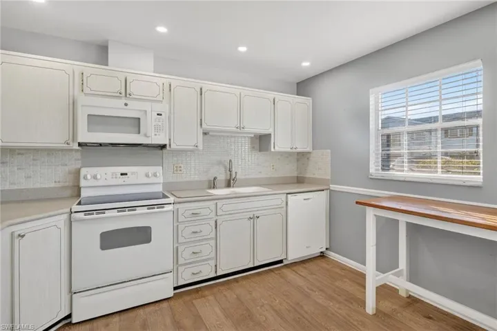 Kitchen featuring white appliances, backsplash, light countertops, light wood finished floors, and recessed lighting